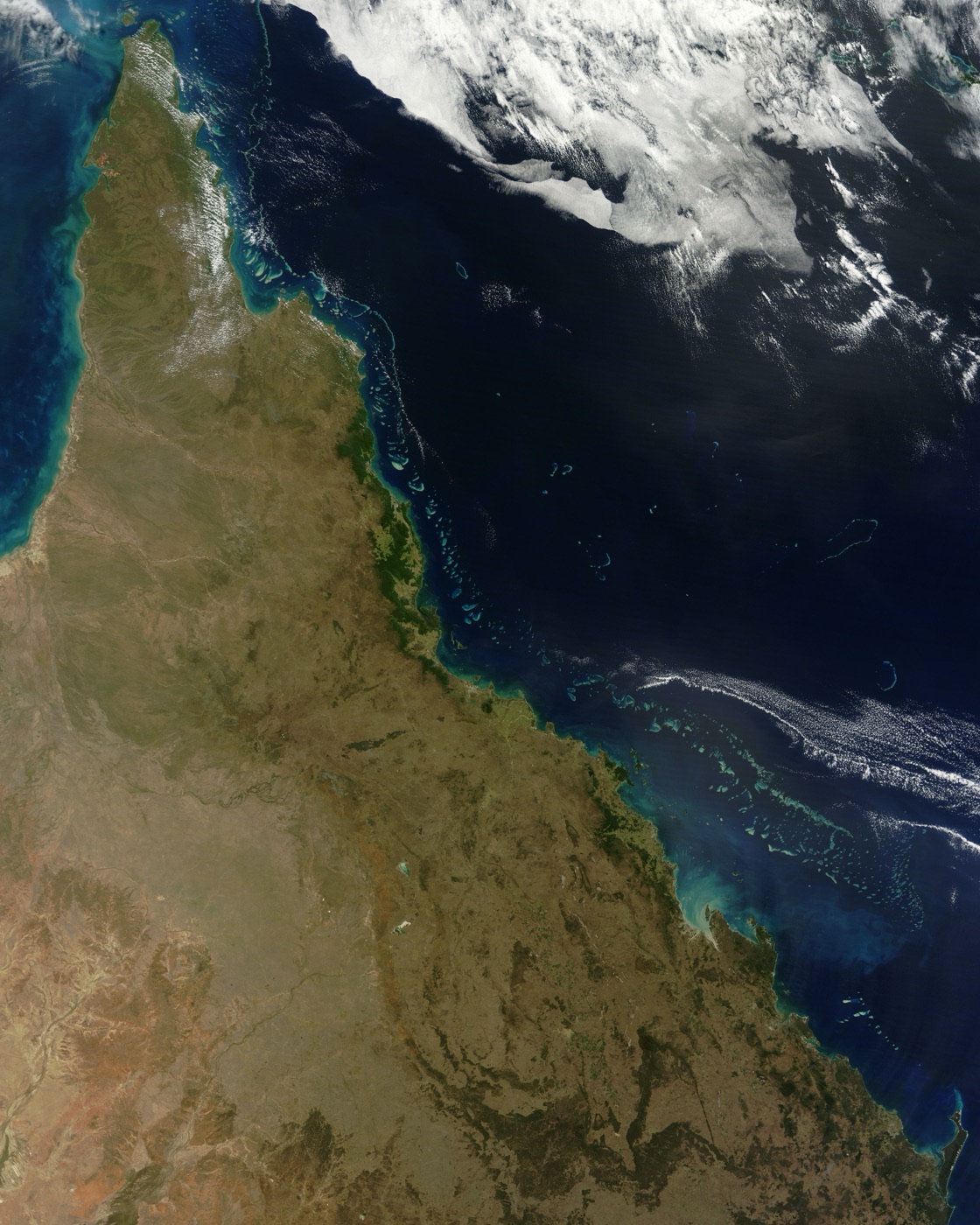 Satellite view of the Australian coast and Great Barrier Reef: turquoise shallows and drowned sandbars visible beneath the water along the shoreline.
